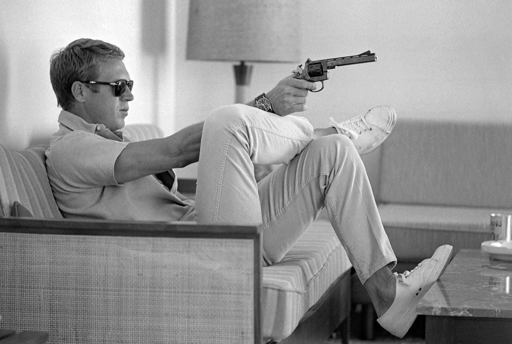 Steve McQueen aims a pistol in his living room.